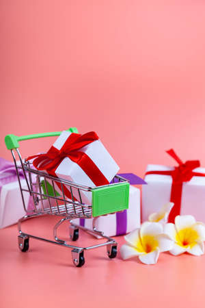 Shopping cart and gifts on a pink background. Concept: buying gifts.の写真素材