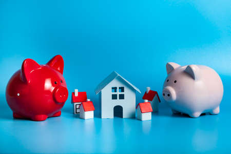 Two pig piggy bank and a small house on a blue background. Real estate purchase concept.の写真素材