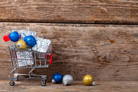Shopping cart with Christmas gifts and balls on a wooden background. Holiday sale.の写真素材