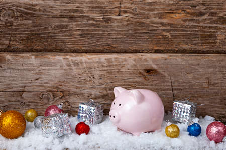 Pig piggy bank and Christmas balls in the snow on an old wooden background. New Year card.の写真素材