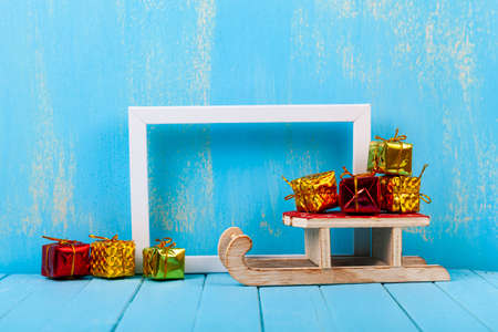 Frame and sleds with gifts on a blue wooden background, place for your text. Christmas card.