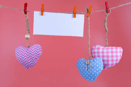 Hearts and a note hang on a rope on a pink background. Valentine's day card.