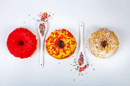 Donuts and spoons with pastry sprinkles on a white background, top view.の写真素材
