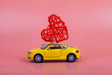 Yellow car with a heart on the roof on a pink background. Valentine's Day card.の写真素材