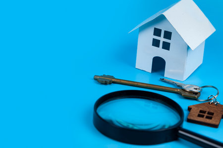 Find a home or a flat concept. Toy model house, magnifying glass and keys. Rent apartments, Real Estate and buying a house idea. blue backgroundの写真素材