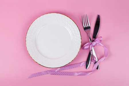 Festive set of cutlery knife and fork with a white dessert plate, pink background, top view, copyspaceの写真素材