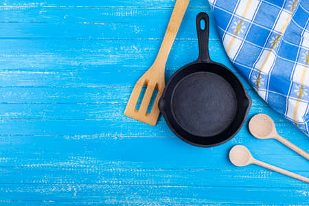 Empty cast iron pan on a blue wooden background. Wooden spatula and kitchen towel. Place for text. flatley.の写真素材