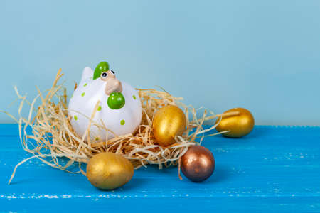 easter greeting card. Easter chick in a nest and colorful eggs. Blue wooden background, place for...
