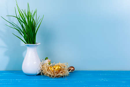 Easter chick in a nest and colorful eggs. White vase with a plant. Blue wooden background, place for your text. easter greeting card.の写真素材