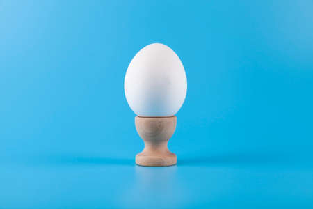 White egg on a wooden stand on a blue background. happy easter.