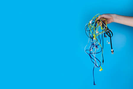 A lot of headphones for a smartphone and a hand on a blue background. Place for your text.の写真素材