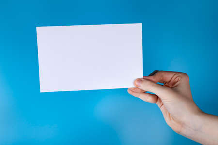 The hand is holding a white sheet of paper. Blue background, copy space.の写真素材