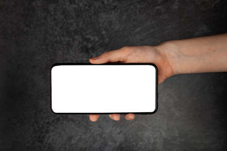 smartphone in hand. White screen, copy space, dark background.の写真素材