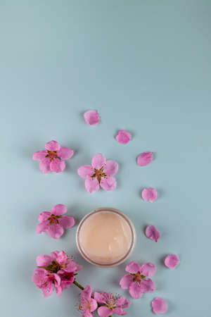 Glass cosmetic jar of cream and decorative pink flowers on a green background. natural organic cosmetics. Spa products for health and beauty. Serum, face oil.の写真素材