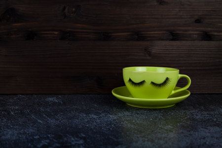 Funny green cup with eyes on a lilac background. False eyelashes are glued to the mug.の写真素材