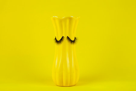 Funny green cup with eyes on a lilac background. False eyelashes are glued to the mug.の写真素材