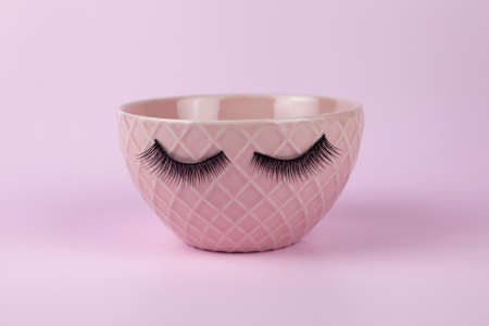 Funny green cup with eyes on a lilac background. False eyelashes are glued to the mug.