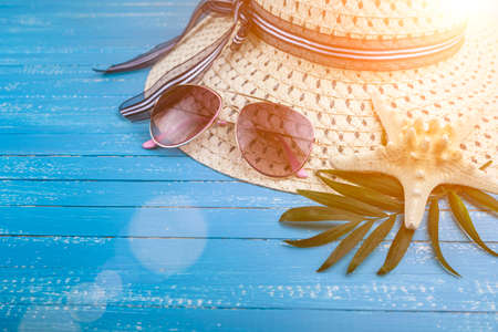 Composition with hat, sunglasses and seashells on a blue wooden background.