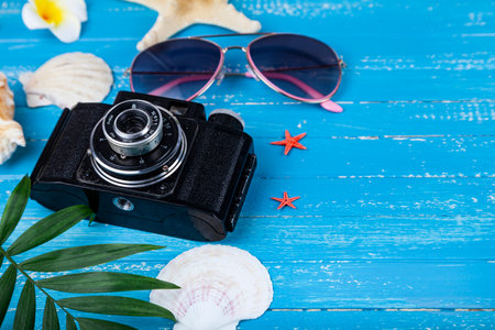 Composition with sunscreen, glasses, camera and seashells on blue wooden background. Everything for a beach holiday.の写真素材