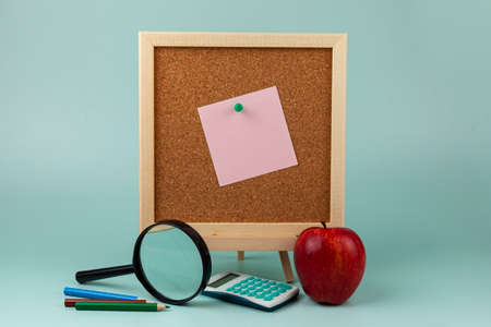 Corkboard with a note, a magnifier, apple and an apple on a green background. Back to school concept.の写真素材