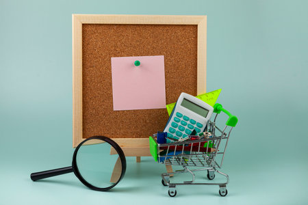 Cork board with note, magnifier and stationery in a shopping cart. shopping for school.の写真素材