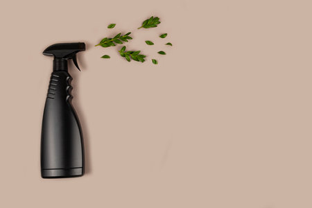 Black bottle mockup for cleaning. Eco spray bottle for safe cleaning with green leaves on pastel brown background. Copy space, flat lay.の写真素材