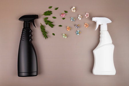 Black and white cleaning bottles. Eco friendly sprayer for safe cleaning with green leaves and flowers on a pastel brown background. Copy space, flat lay.の写真素材