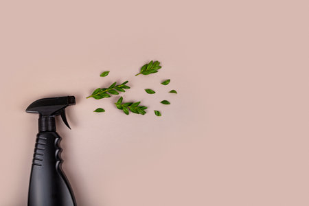 Black bottle mockup for cleaning. Eco spray bottle for safe cleaning with green leaves on pastel brown background. Copy space, flat lay.の写真素材
