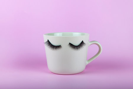 Funny white mug with eyes on a pink background. False eyelashes are glued to the mug.の写真素材