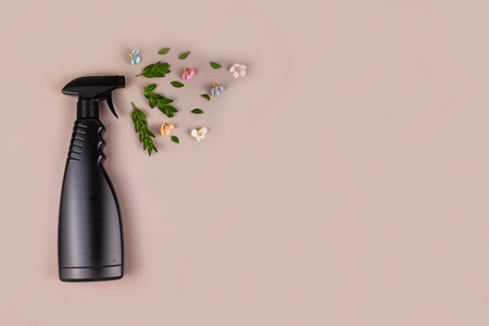 Black cleaning bottle. Eco friendly sprayer for safe cleaning with green leaves and flowers on a pastel brown background. Copy space, flat lay.の写真素材