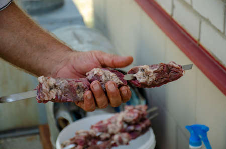 A man puts pieces of barbecue on a skewer in the process of cooking barbecue outdoorsの写真素材