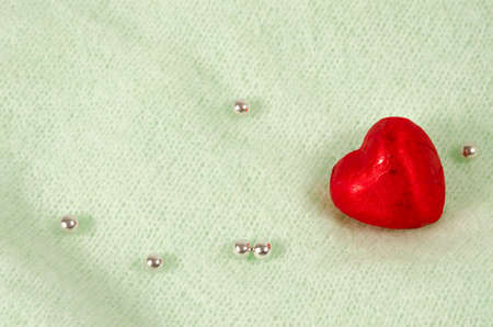 Chocolate heart in a red wrap on a light background with shiny beads. Valentine's Day