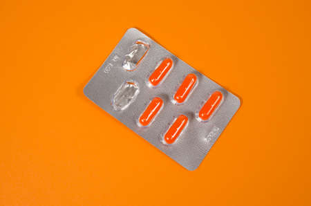 Bright orange tablets in silver packaging on an orange background