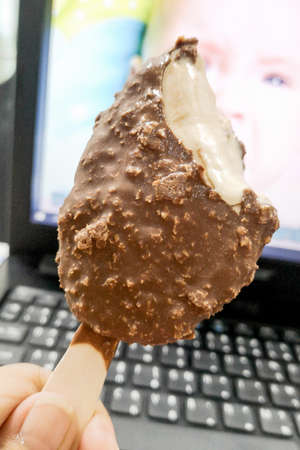 Hand holding bitten chocolate ice cream infront of keyboard background.の写真素材