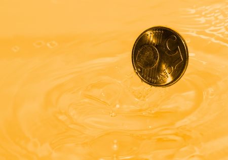 A euro coin drops into a gold liquidの写真素材