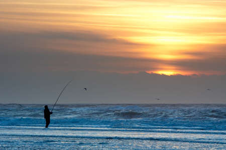 A man fishing on the beach at sunsetの写真素材