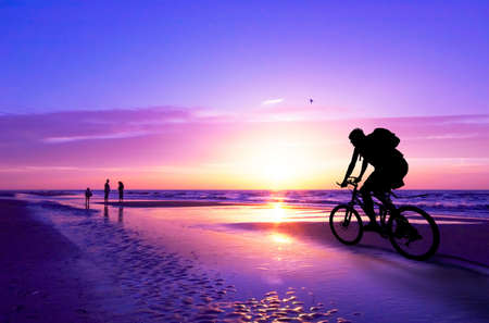 silhouette of a mountain biker on beach and sunsetの写真素材