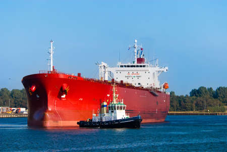 A huge red oil tanker and a tugboat at workの写真素材
