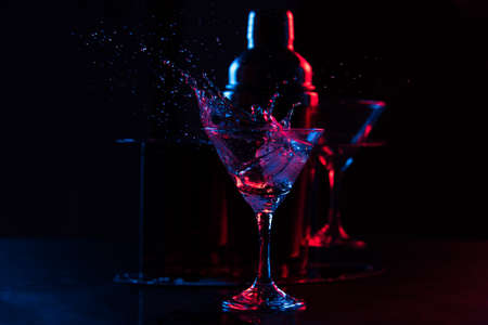 glass of cocktail with splashes on black background with red and blue lightsの写真素材