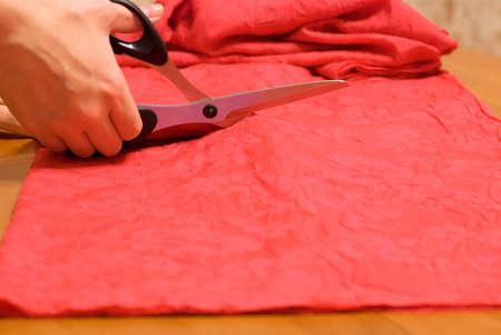 Hand cut red fabric with scissors on tableの写真素材