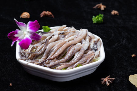 Fresh raw squid in a white bowl on a black background with herbsの写真素材