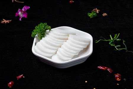 Slices of white food in white bowl on black backgroundの写真素材