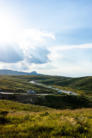 mountain road in summer under blue sky with clouds and sun raysの写真素材
