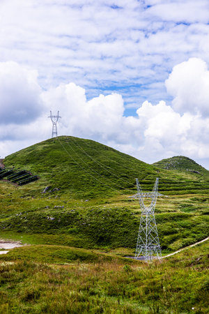 High voltage power lines in the mountains with green grass and blue skyの写真素材