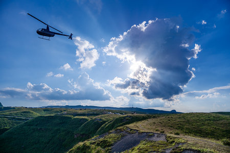 Helicopter flying over the mountains under a blue sky with cloudsの写真素材