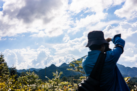 Man taking photo of beautiful mountain landscape with blue sky and white clouds.