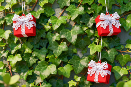 Red gift boxes with white ribbons hanging on green ivy wallの素材