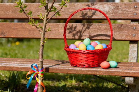 Colorful Easter eggs in a basket on a wooden bench in the gardenの素材