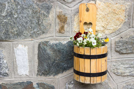 A wooden pot of flowers hang on stone wallの写真素材