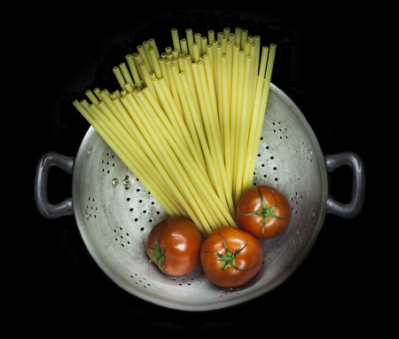 Colander with pasta and three tomatoes isolated on a black background
の写真素材